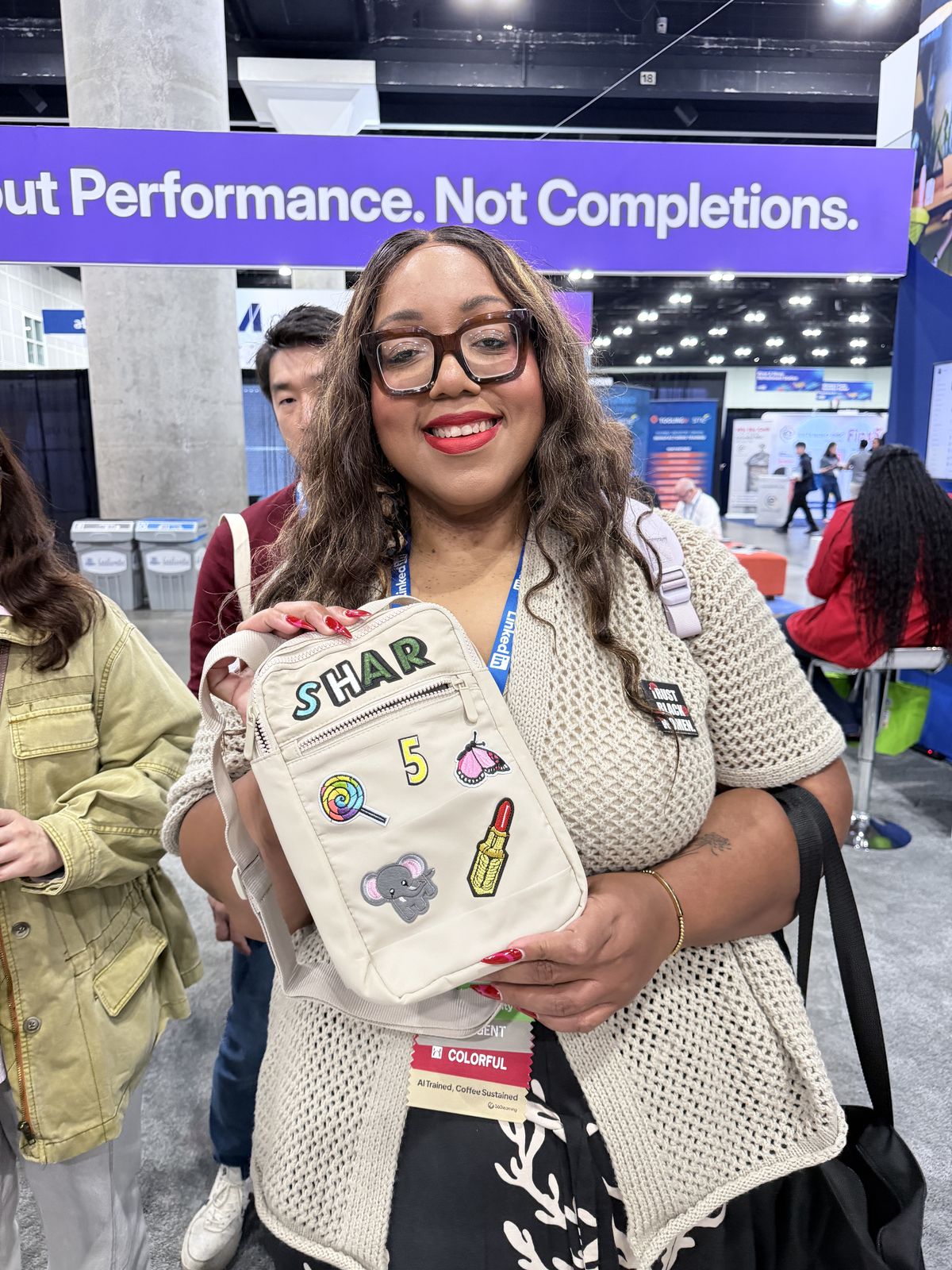 Smiling conference guest holding a cream crossbody bag customized with name letters and novelty patches