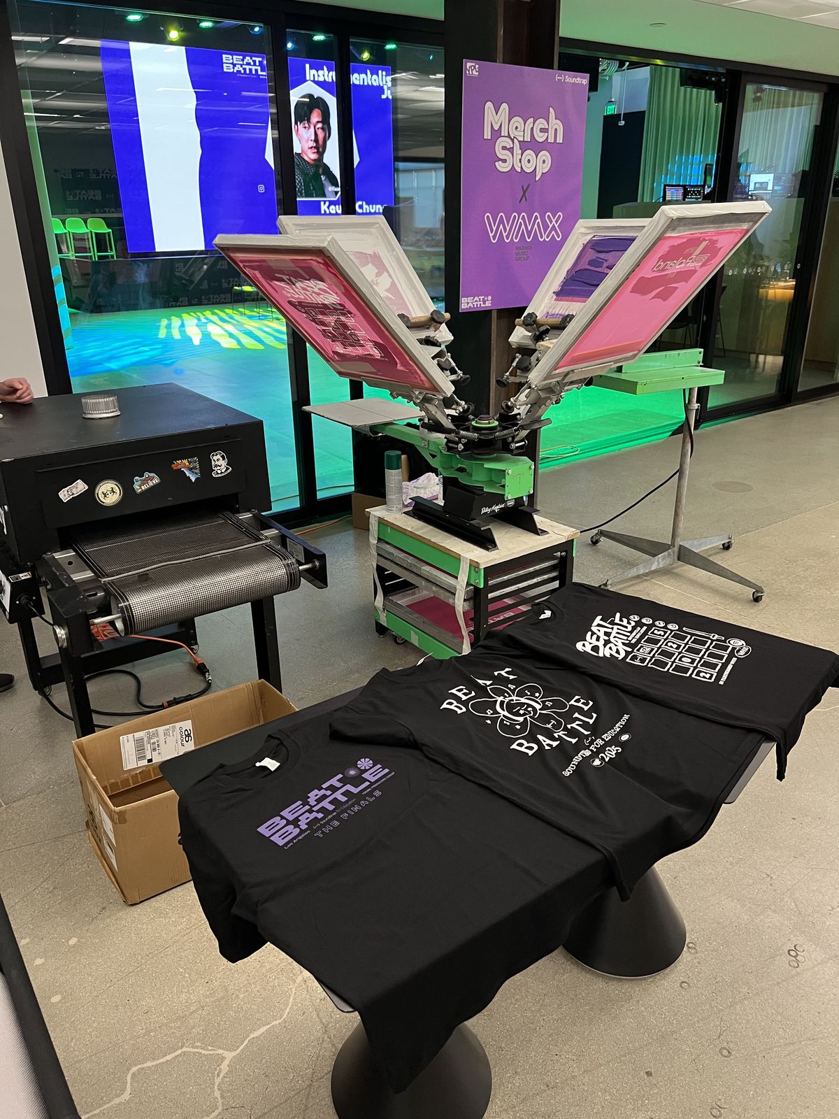 Live customization stop with pink screens and finished black tees laid out at a Los Angeles music industry event
