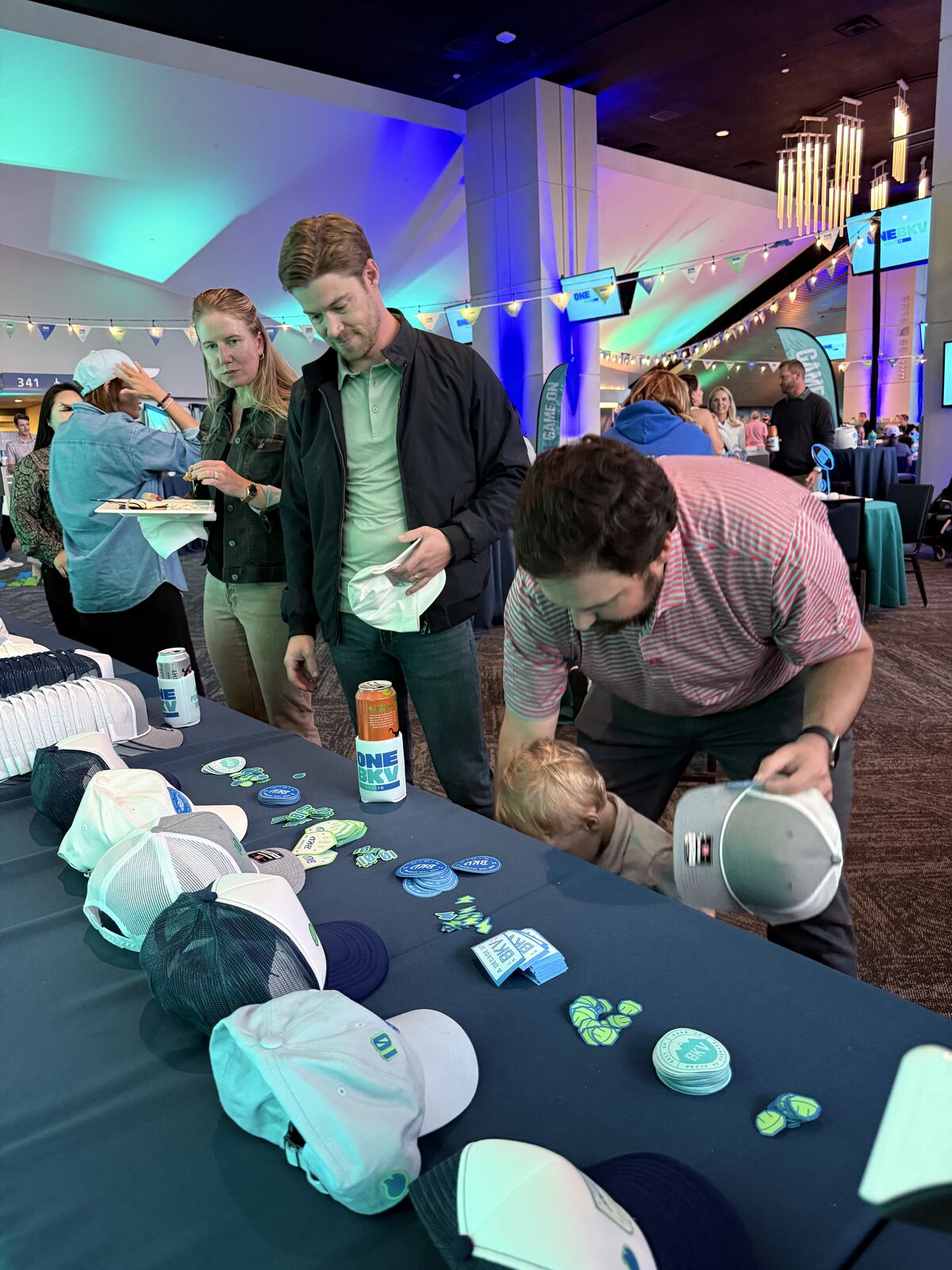 Guests browsing trucker caps and embroidered patches spread across a navy hat bar table at a stadium club event